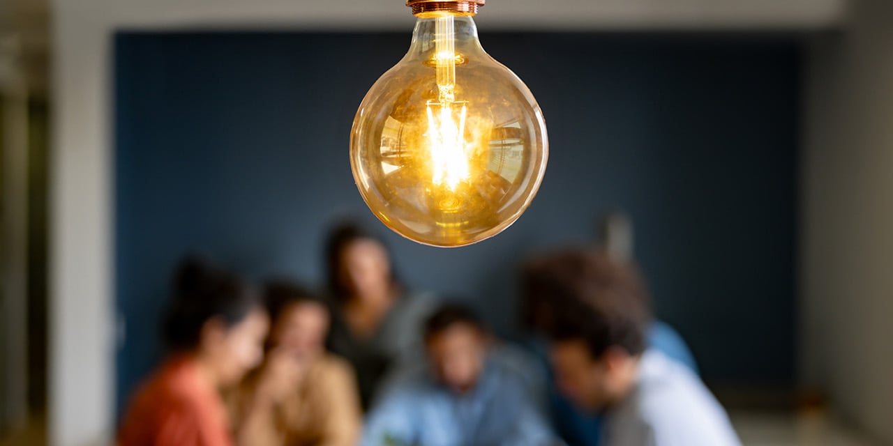 Lightbulb featured image with blurred background of a group of people at a table.
