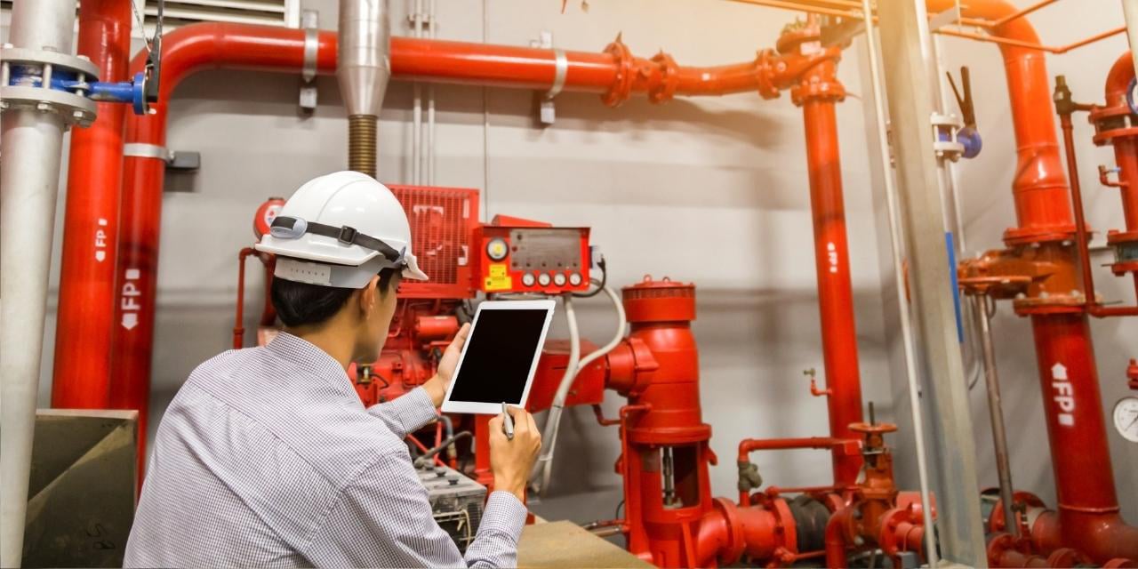 Man with iPad inspecting fire safety equipment.