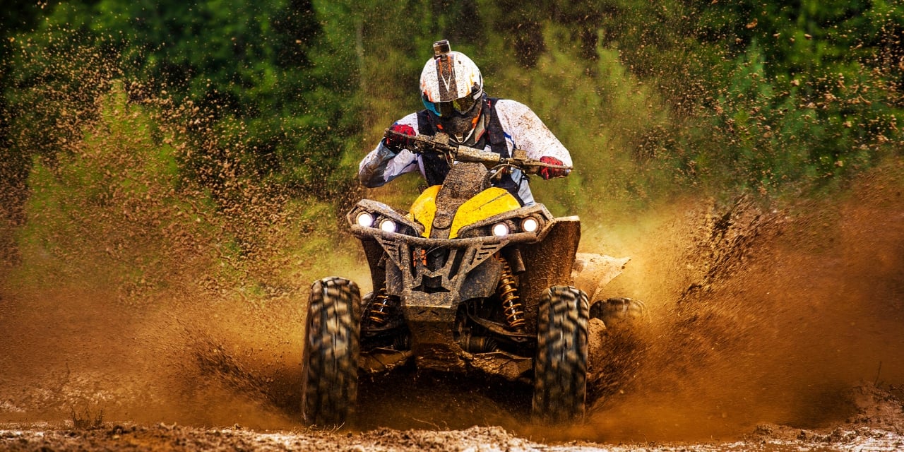 Person driving an ATV through splashing mud.