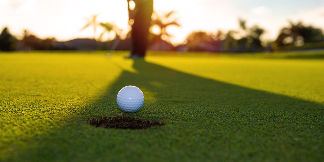 White golf ball rolling into the hold on the green.