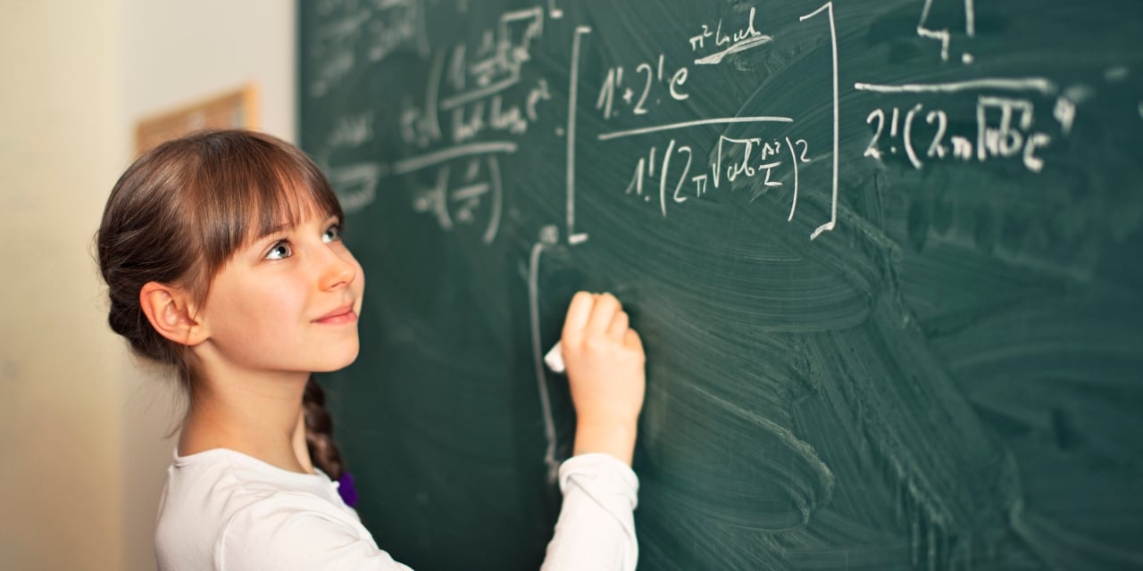 Student completing a math equation on a chalkboard.